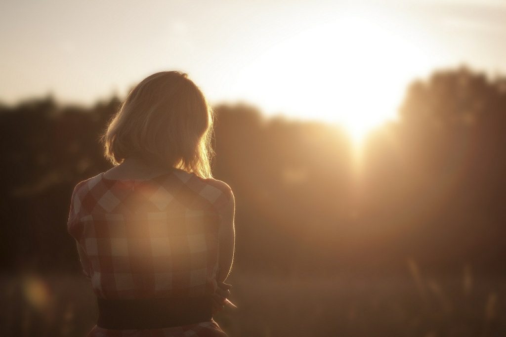 Person with shoulder length hair has back to camera and faces the sunset